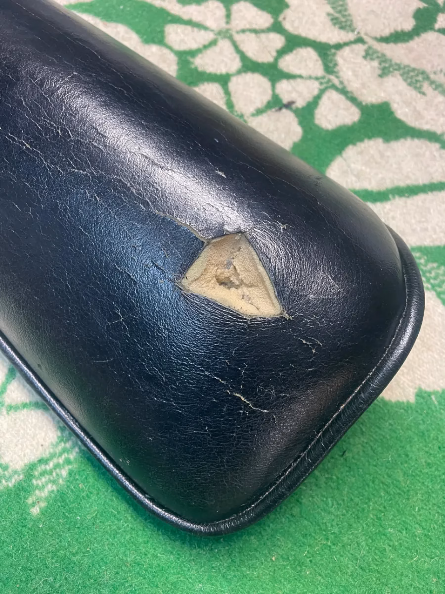 Black leather cushion with a hole and surface cracking, before repair by Apex Leather Repair