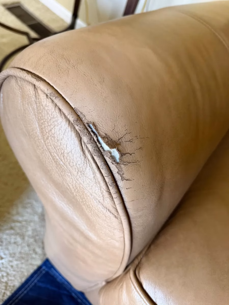 Tan leather sofa arm with a tear and cracking along the seam, before repair
